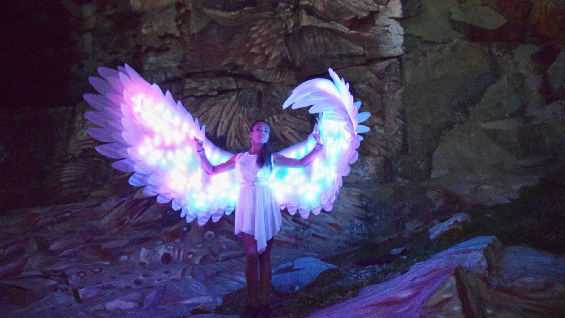 El Ángel de Luz: Un Espectáculo de Fuego y Magia Artista vestida de ángel con alas iluminadas actuando en un impactante espectáculo de fuego y luces.